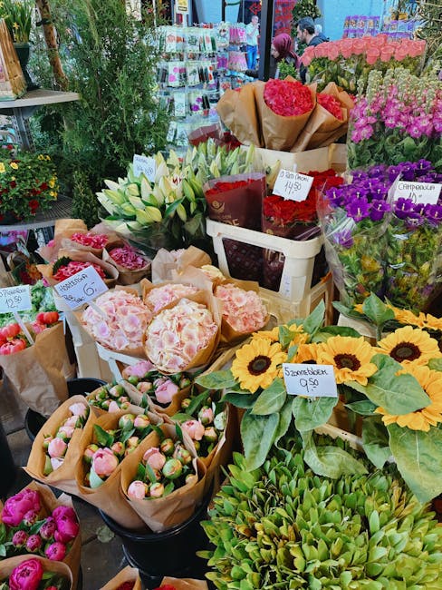 A vibrant display of fresh flowers at Hackney Florist, including sunflowers with large, bright yellow petals and dark centers, white lilies with elongated petals and green stems, and various pink and 