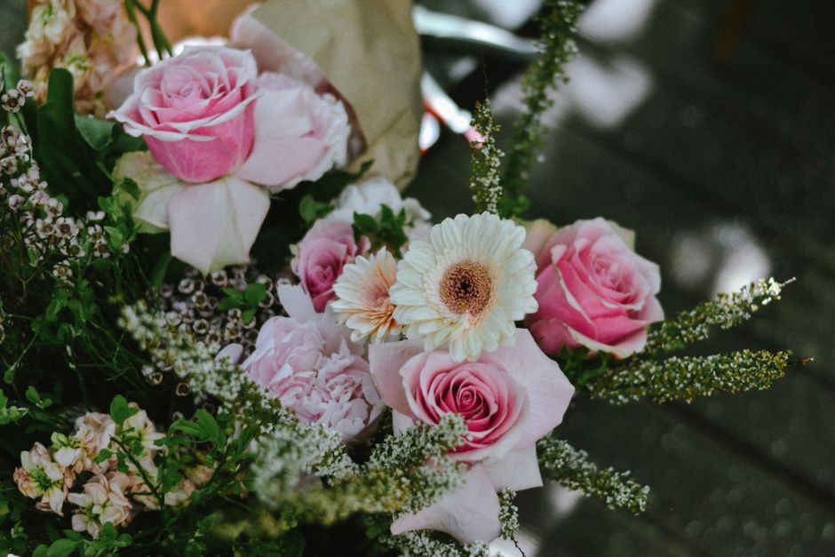 A floral arrangement featuring a bouquet of fresh pink roses with tightly closed and partially opened petals, complemented by white gerbera daisies with brown centers, surrounded by delicate white and